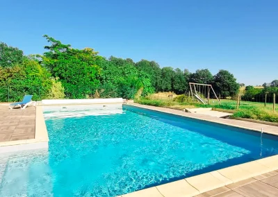 Piscine partagée de la Ferme de Menoun avec transats et balançoire dans le fond.